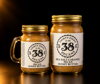 38 Pecans classic Pecan Honey Butter and Sea Salt Caramel Pecan Honey Butter in gold-lidded glass jars against a black studio background.