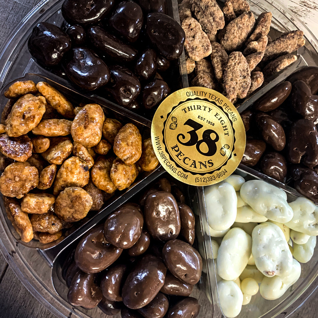 A clear plastic container with compartments, filled with an assortment of chocolate-covered and honey toasted pecans. The container has a gold label with '38 PECANS' branding.